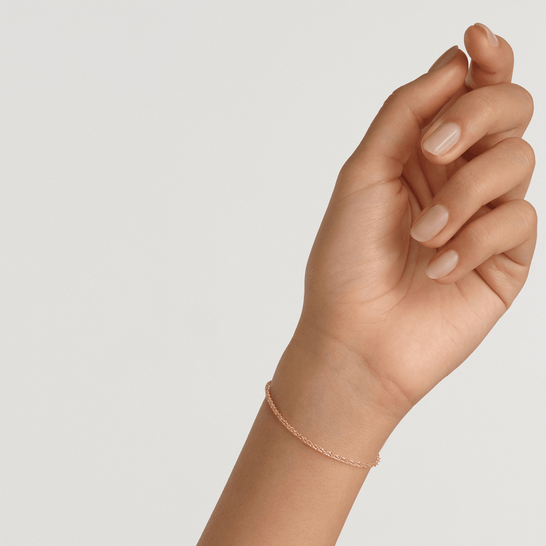 A woman’s wrist wearing the Twisted Chain Bracelet G, showing its slim twisted gold chain design and delicate fit, ideal for everyday elegance and layering with other jewellery.