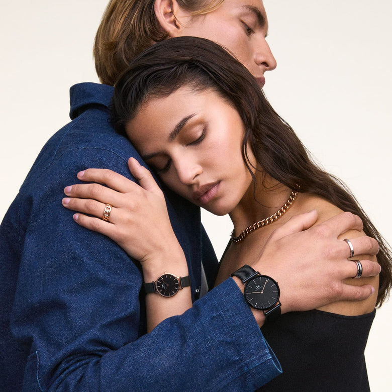 A woman wearing the Petite Ashfield Rose Gold ladies watch with a black mesh strap and rose gold case, styled for a modern, elegant look while embracing a partner.