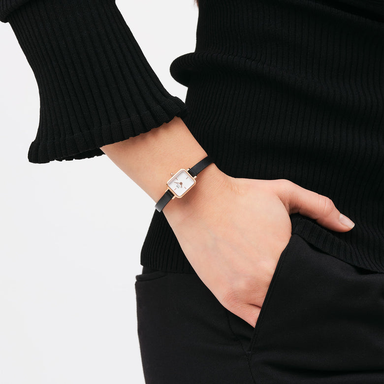 A woman wears the Quadro Mini Sheffield Rose Gold watch with a petite rectangular rose gold case, minimalist white dial, and slim black leather strap, styled for everyday comfort and understated elegance.