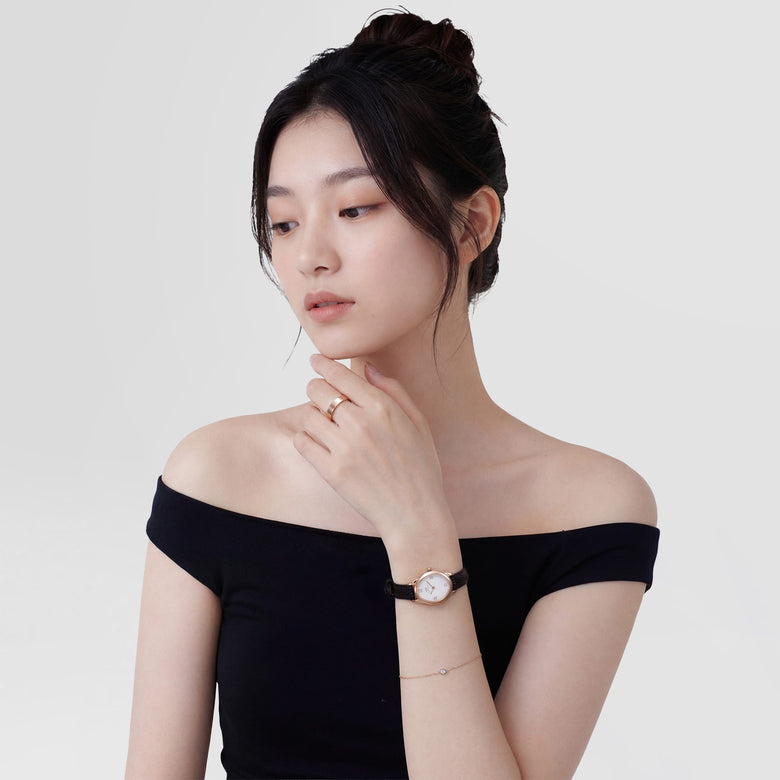 A woman wearing the Ophelia Mini Black Lizard White Guilloché Rose Gold watch, featuring a petite rose gold case, white guilloché dial with Roman numerals, and a textured black leather strap, styled with a minimalist black top for a modern and elegant look.