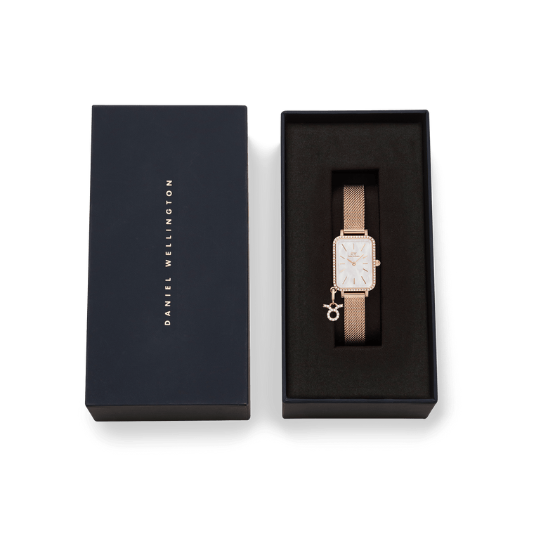 Quadro Crystal Zodiac Melrose ladies watch with rose gold mesh strap, crystal-framed rectangular case, and zodiac charm, presented in a branded Daniel Wellington gift box.