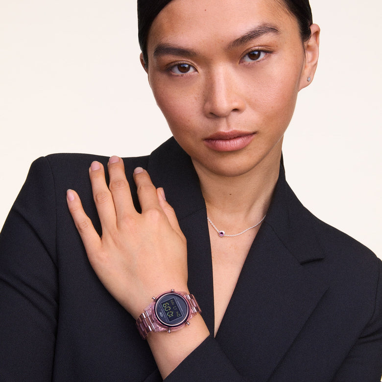 A woman wearing the Retro Digital Dark Pink Dark Pink watch with a transparent bio-based plastic strap and black digital dial, styled with a dark blazer and delicate necklace for a modern, professional look.