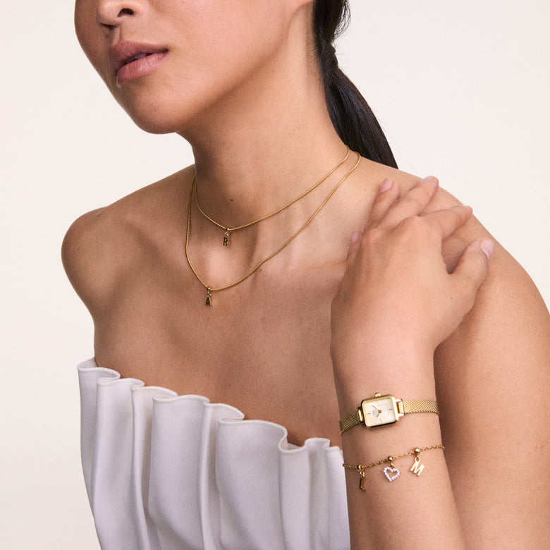 A woman wearing the Quadro Mini Evergold Champagne gold watch with a rectangular case and champagne dial, styled alongside a gold charm bracelet and layered gold necklaces, highlighting its elegant fit for petite wrists and versatility for both casual and formal outfits.