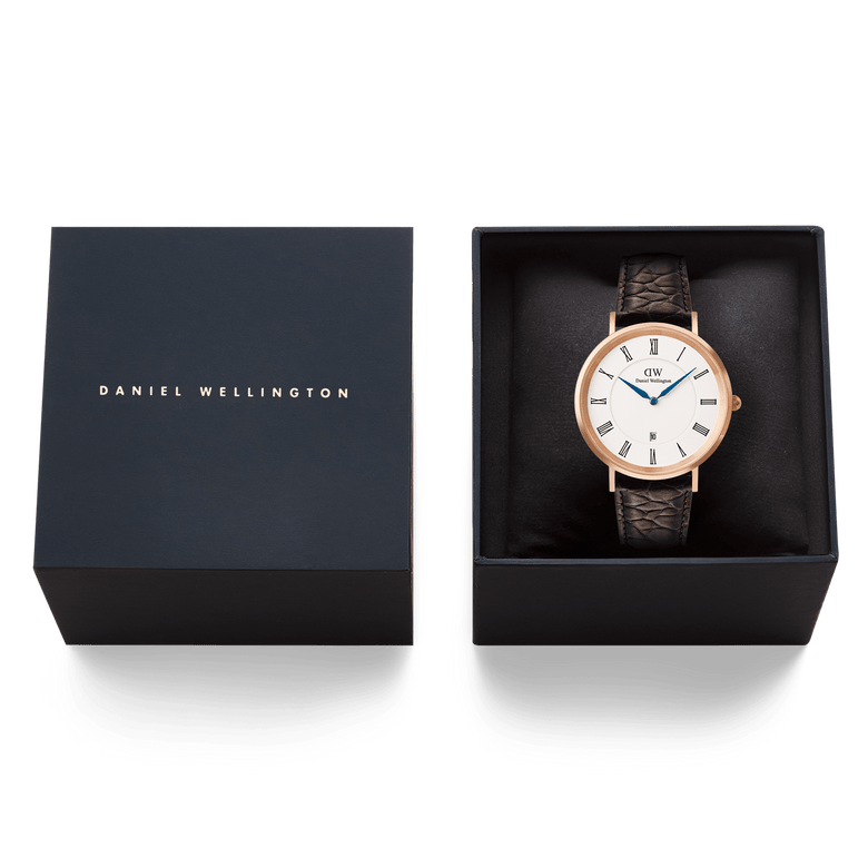 Classic Roman Numerals Date Dark Brown Croc Belly Rose Gold men’s watch presented in a black Daniel Wellington gift box, featuring a rose gold case, white dial with Roman numerals, blue hands, and a brown croc-embossed leather strap.