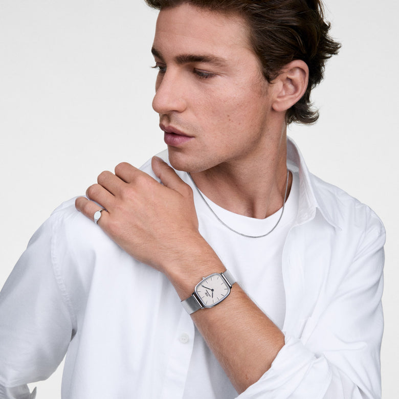 A man wearing the Marlon Wire Linen Silver watch with a rectangular stainless steel case, soft yellow linen-textured dial, and silver mesh strap, styled with a white shirt and silver jewellery for a modern, versatile look.