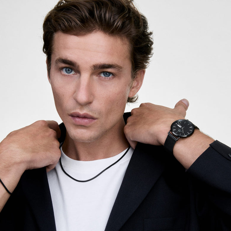 A person wearing the Tide Mesh Necklace Black 2.8 styled with a white T-shirt and dark blazer, showcasing the necklace’s sleek mesh chain and modern, minimal look.