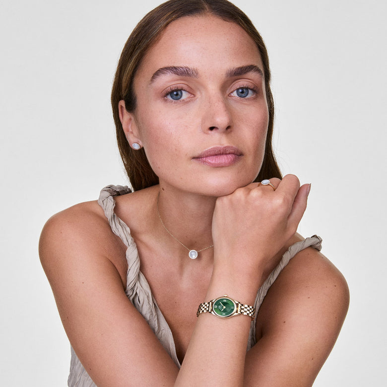A woman wearing the Audrey Necklace Mother of Pearl Gold, featuring a delicate gold chain and a round mother of pearl pendant with a halo of cubic zirconia crystals, styled with a sleeveless top for a refined, everyday look.
