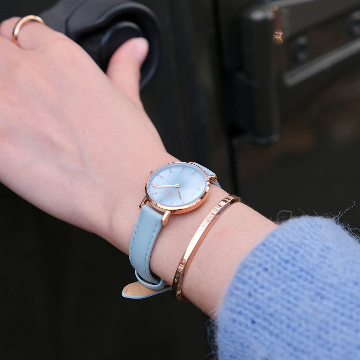 Petite Bluebell ladies watch with a pastel blue leather strap and rose gold case, worn on the wrist alongside a rose gold bangle, highlighting its elegant and versatile style for everyday wear.
