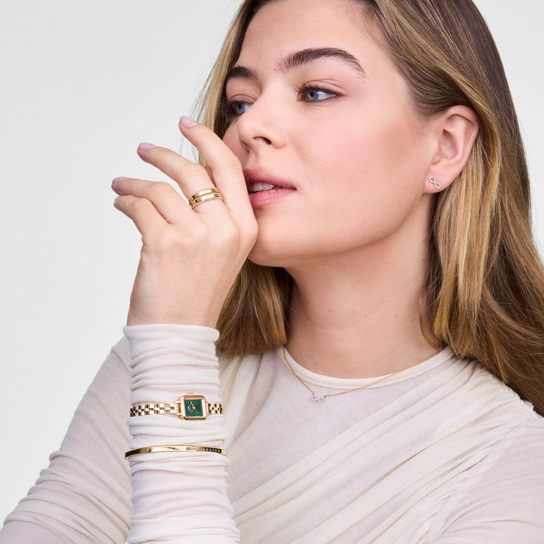 A woman wearing the Quadro Mini Arch 3-link Emerald Sunray Gold watch on her wrist, styled with gold jewellery and a cream long-sleeve top, highlighting the petite gold bracelet and emerald green rectangular dial for a modern, elegant look.