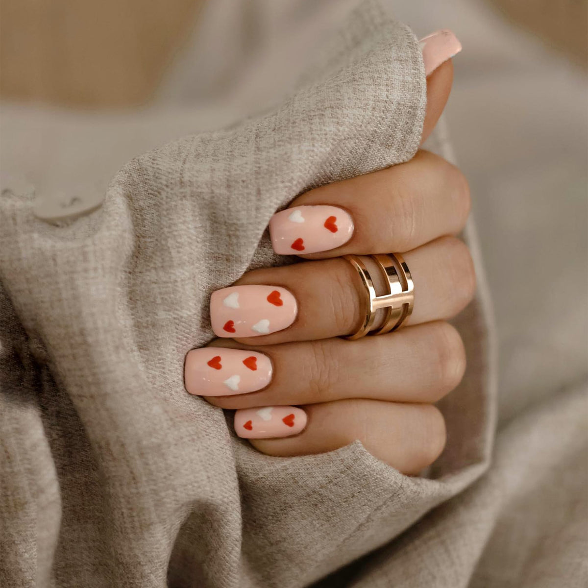 Elan Triad Ring Rose Gold with a triple band design worn on a woman's hand, styled with pink nail polish and red and white heart accents, creating a modern and elegant look.