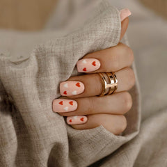 Elan Triad Ring Rose Gold with a triple band design worn on a woman's hand, styled with pink nail polish and red and white heart accents, creating a modern and elegant look.