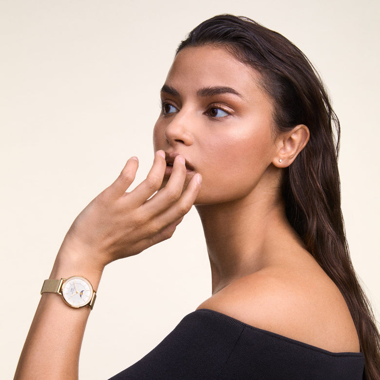 A woman wearing the Petite Lune Evergold ladies gold watch with a mesh strap and moon-phase dial, styled with a black off-shoulder top for a modern, everyday look.