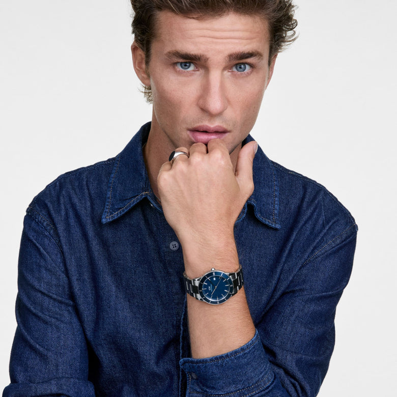 A man wearing the Iconic Paradigma Link Blue Enamel Silver watch with a blue enamel dial and stainless steel bracelet, styled with a casual denim shirt for a modern everyday look.