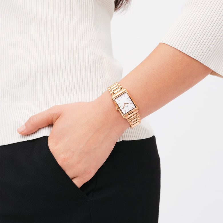 Bound 3-Link Rose Gold watch with a rectangular case and white dial, worn on the wrist with a polished rose gold 3-link bracelet, styled with a white top and black trousers for a modern, everyday look.