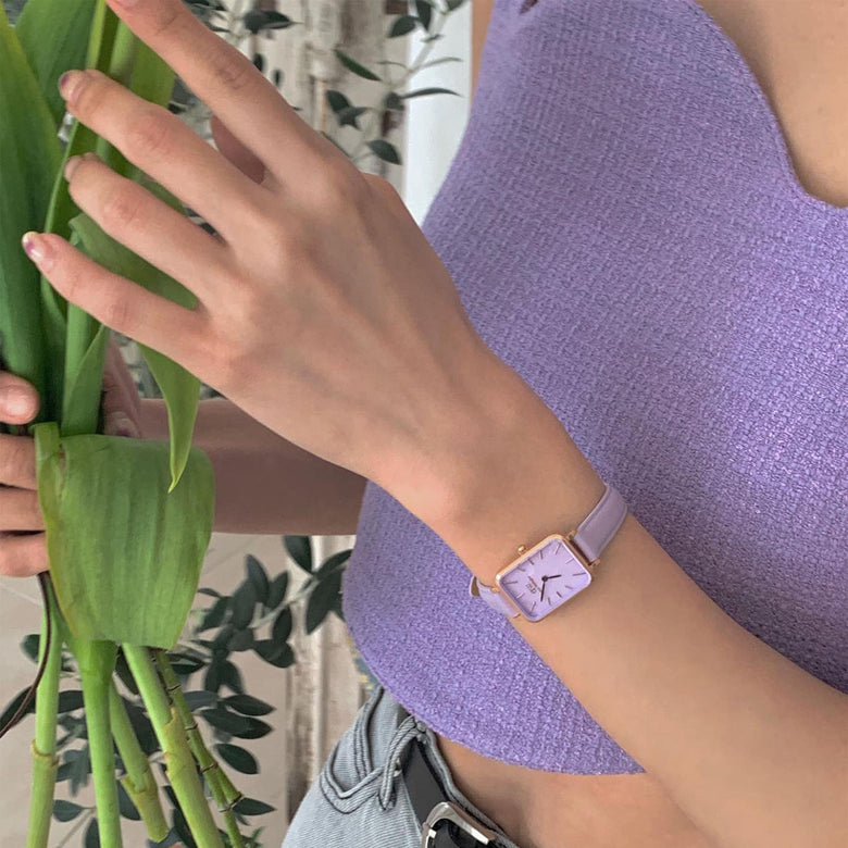 Quadro Lavender MOP Rose Gold ladies watch with a rectangular rose gold case and pastel purple leather strap, worn with a matching lavender top while holding fresh green leaves.