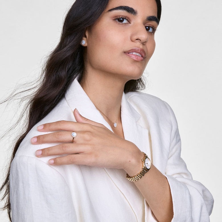 A woman wearing the Ophelia Mini Gold watch with a gold oval case and polished link bracelet, styled with a white blazer and matching gold jewellery for a refined, everyday look.