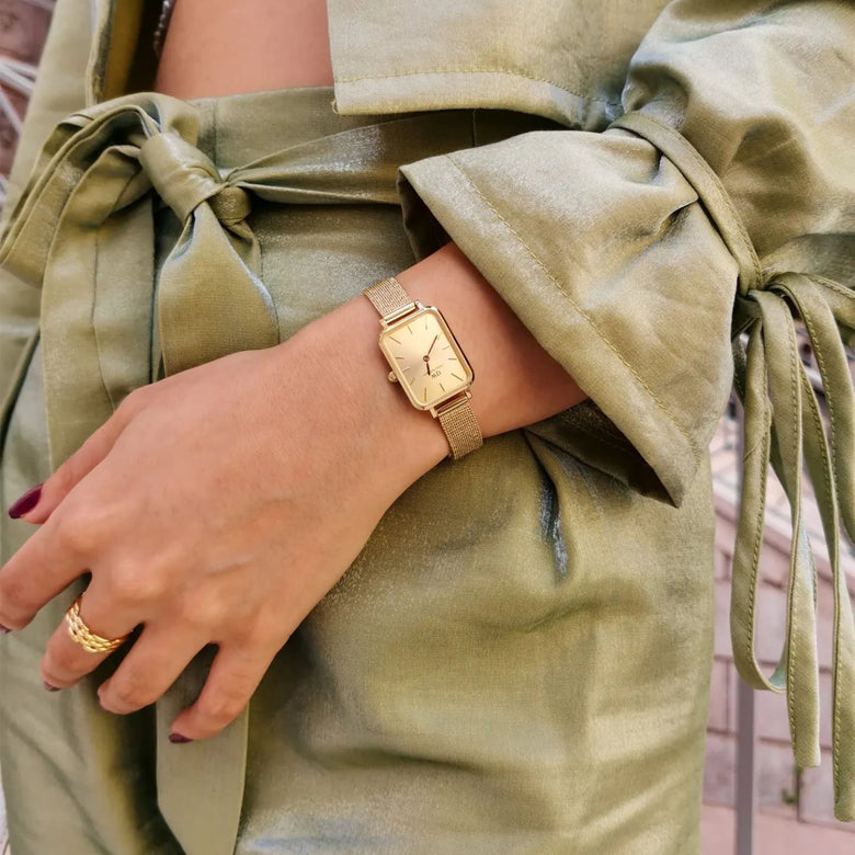 Quadro Pressed Unitone Gold women’s watch with a rectangular gold dial and pressed mesh strap, worn with a light green satin outfit for a chic, sophisticated look.