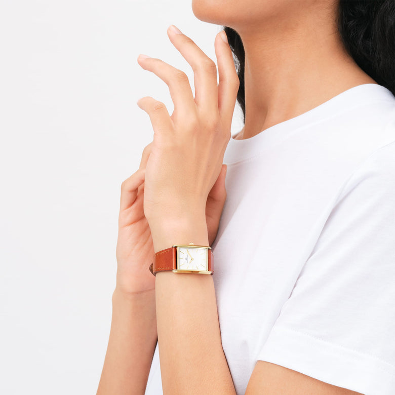 A woman wearing the Bound Durham Gold watch, featuring a rectangular gold case, minimalist white dial, and light brown leather strap, styled with a casual white top for a modern everyday look.