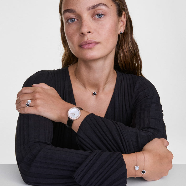 A woman wears Audrey Earrings Black Agathe Rose Gold, styled with matching black agate and rose gold jewellery including a necklace, ring, bracelet, and watch, creating a coordinated and elegant look suitable for both formal and everyday occasions.