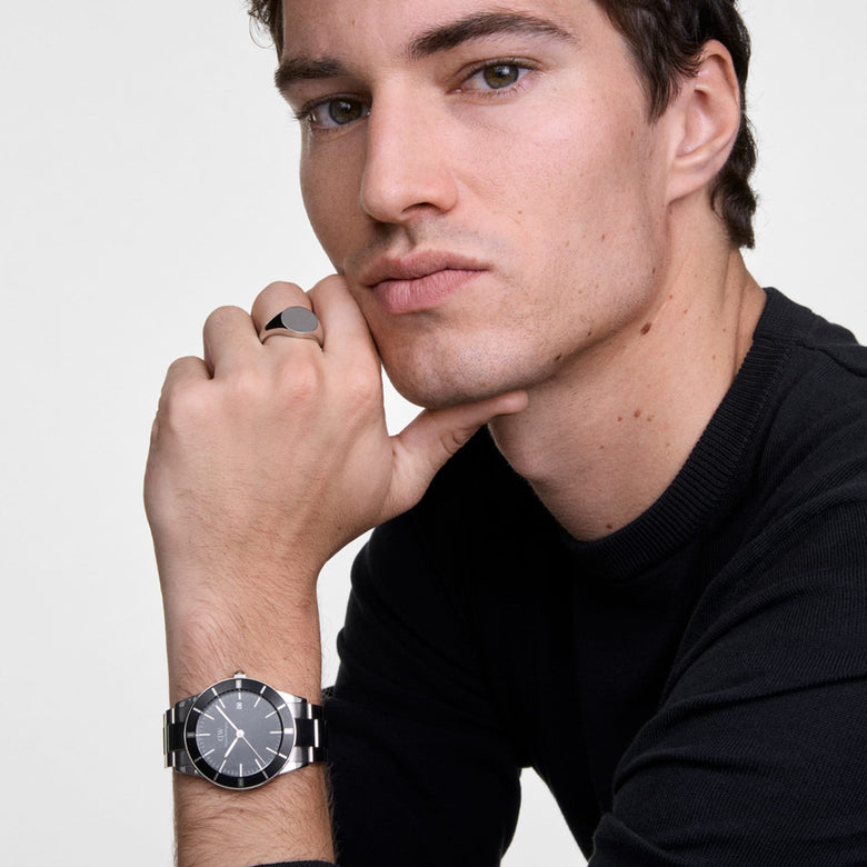 A man wearing the Iconic Paradigma Link Black Enamel watch, showing its silver stainless steel bracelet, minimalist black dial, and distinctive index bezel paired with a casual black top for a modern, versatile look.