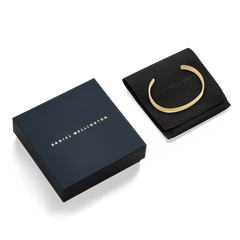 Line Cuff Polished Gold bracelet displayed on a black pouch next to a navy Daniel Wellington gift box, highlighting its elegant gold finish and premium packaging ideal for gifting.