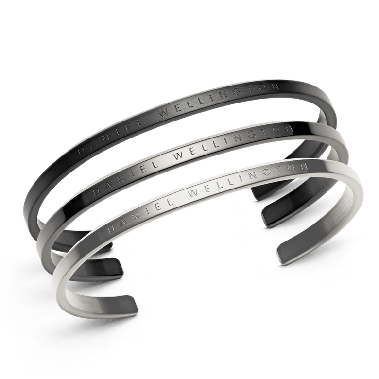 Three Daniel Wellington Classic Bracelets in black, graphite, and silver tones, each featuring a slim stainless steel cuff design with engraved branding and a smooth, minimalist finish.