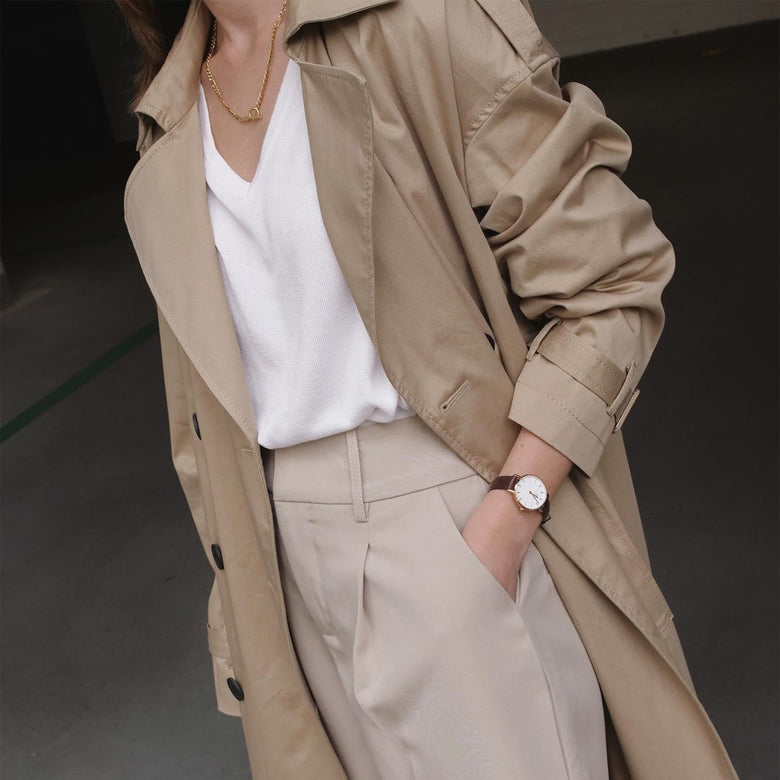 A woman wearing the Petite St Mawes rose gold watch with a brown leather strap, styled with a beige trench coat and tailored trousers for a polished, everyday look.
