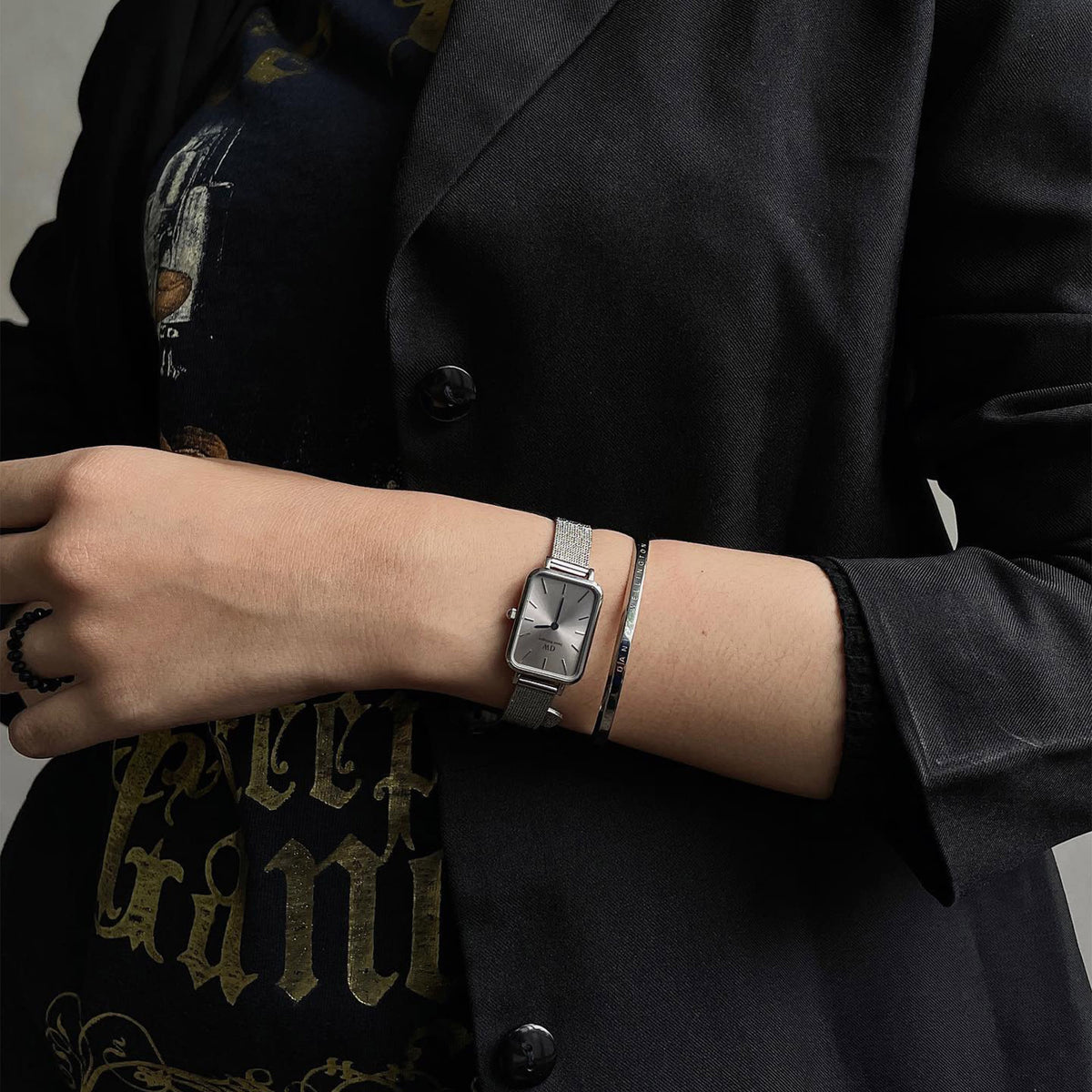 Quadro Pressed Unitone Silver ladies watch with a rectangular brushed silver dial and mesh strap, worn alongside a silver bracelet and styled with a black blazer for a modern, understated look.