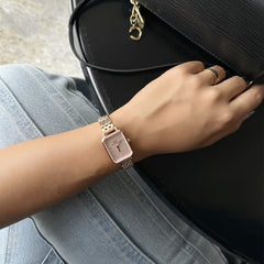 A woman wearing the Quadro Lumine 5 Link Melrose Pink MoP Rose Gold watch, featuring a rectangular pink mother of pearl dial and rose gold five-link bracelet, styled with casual denim and a black handbag.