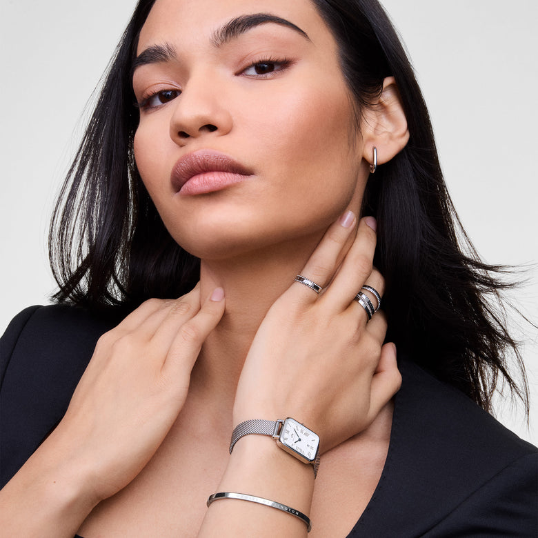Woman wearing the Quadro Sterling Roman Numerals Date ladies watch with a rectangular silver mesh strap, white dial, Roman numerals, and blue hands, styled with silver jewellery for a modern, elegant look.