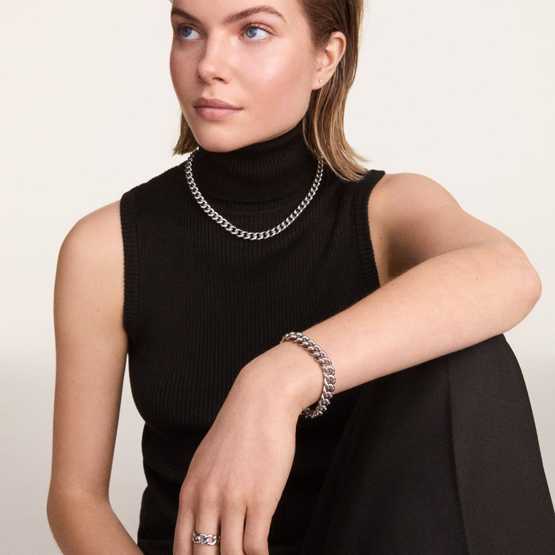 A woman wears the Chunky Chain Bracelet Silver on her wrist, styled with a matching silver chain necklace and ring, paired with a black sleeveless top for a modern, sophisticated look.