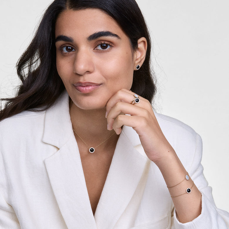 Audrey Earrings Black Agathe Gold worn with matching jewellery, featuring domed black agate centres surrounded by cubic zirconia crystals in a gold setting, styled with a white blazer for a polished, modern look.