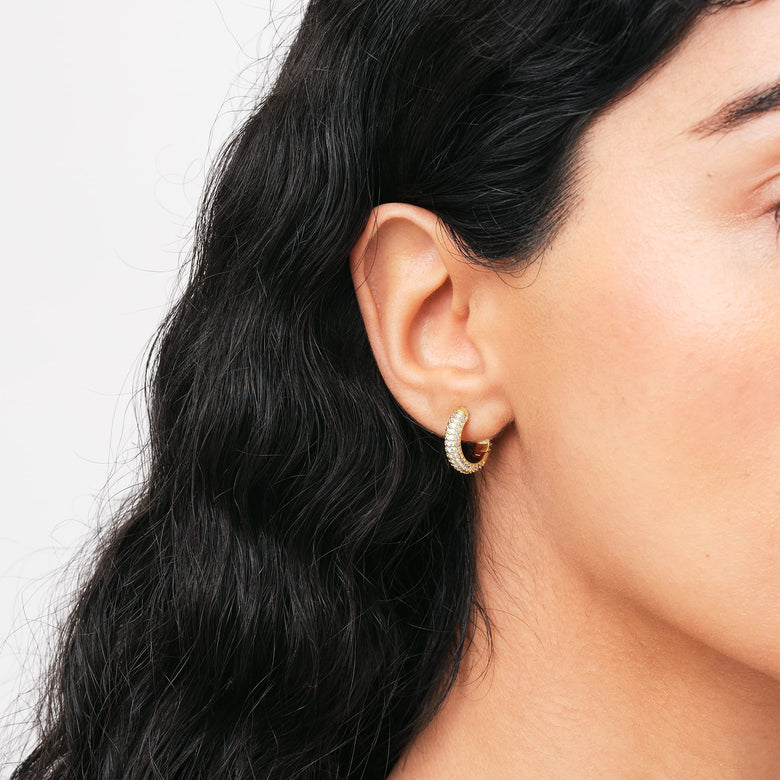 A woman wearing the Pavé Crystal Earrings Gold, featuring a compact gold hoop encrusted with sparkling cubic zirconia crystals, styled for everyday elegance.
