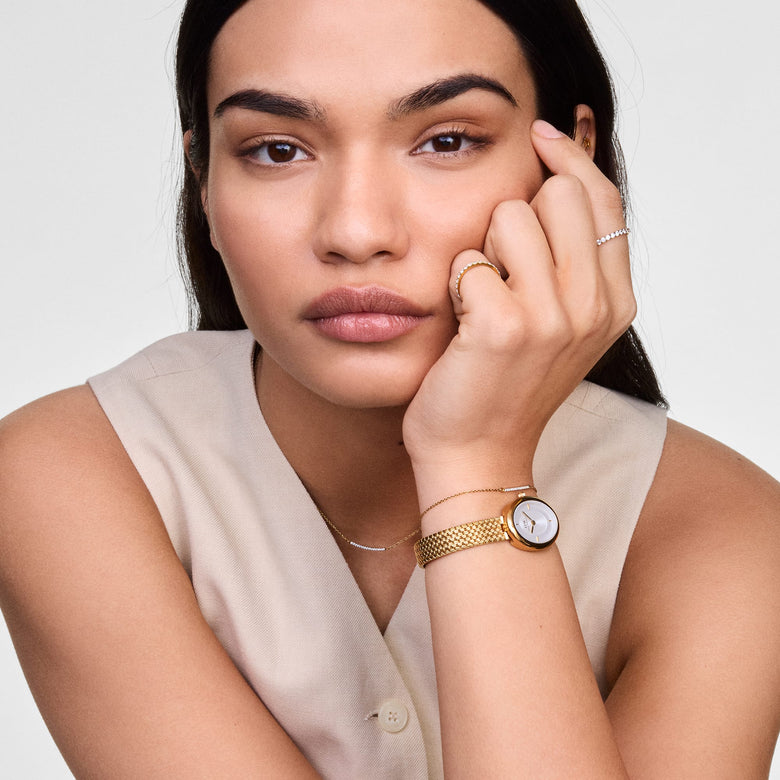 A woman wearing the Juliette Braided Mesh White Sunray Gold watch, featuring a gold braided mesh strap and oval white sunray dial, styled with neutral clothing and delicate jewellery for a modern, understated look.