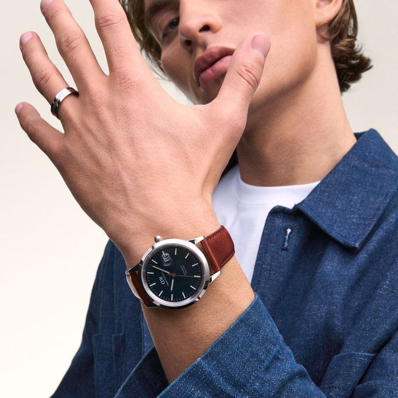 A man wearing the Iconic St Mawes Automatic Silver watch with a brown Italian leather strap and arctic blue enamel dial, styled with a denim shirt and white T-shirt for a smart casual look.