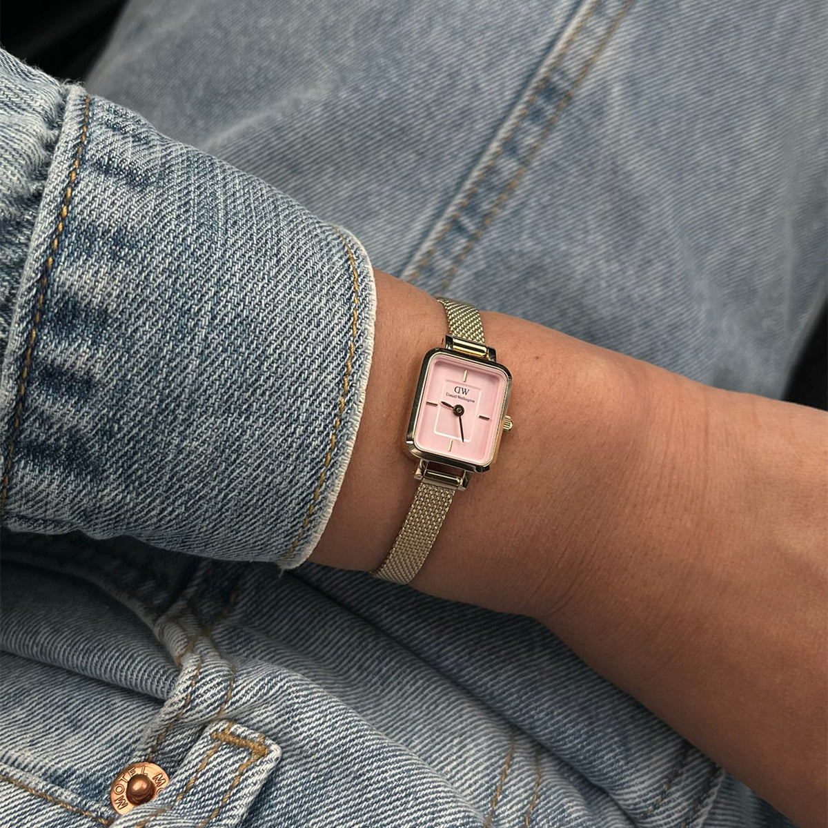 Quadro Mini Evergold Blush gold watch with a blush pink dial and gold mesh strap, worn on a wrist paired with a light blue denim jacket for a casual, stylish look.