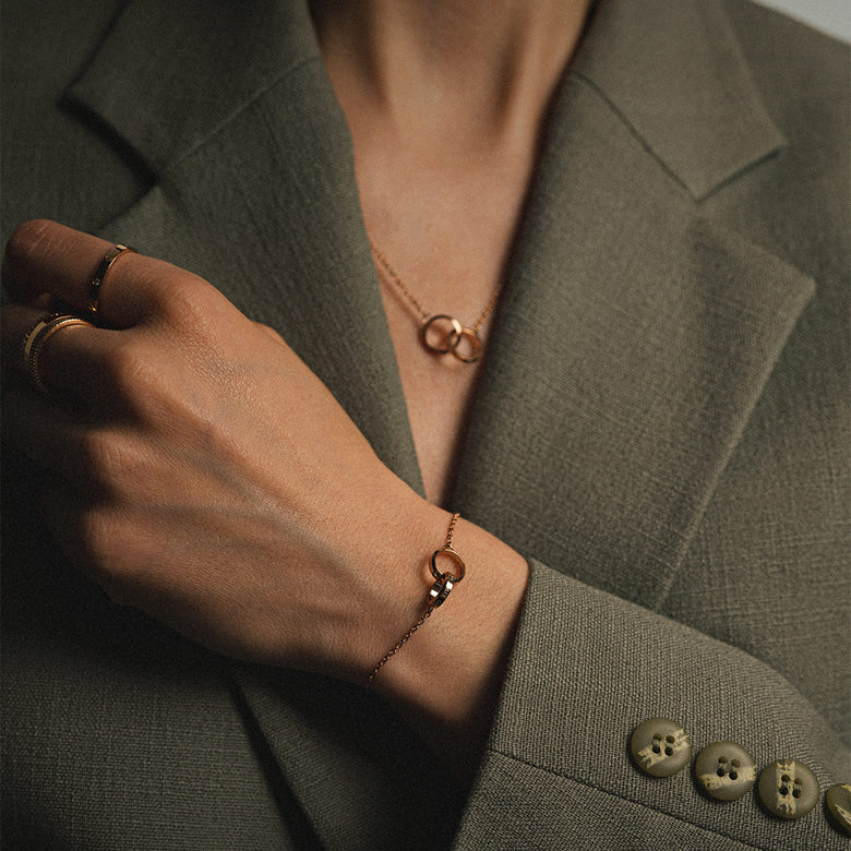 Woman wearing the Elan Unity Bracelet Rose Gold with two interlocking rings on a slim chain, styled with a matching necklace and gold rings for a classic, elegant look.