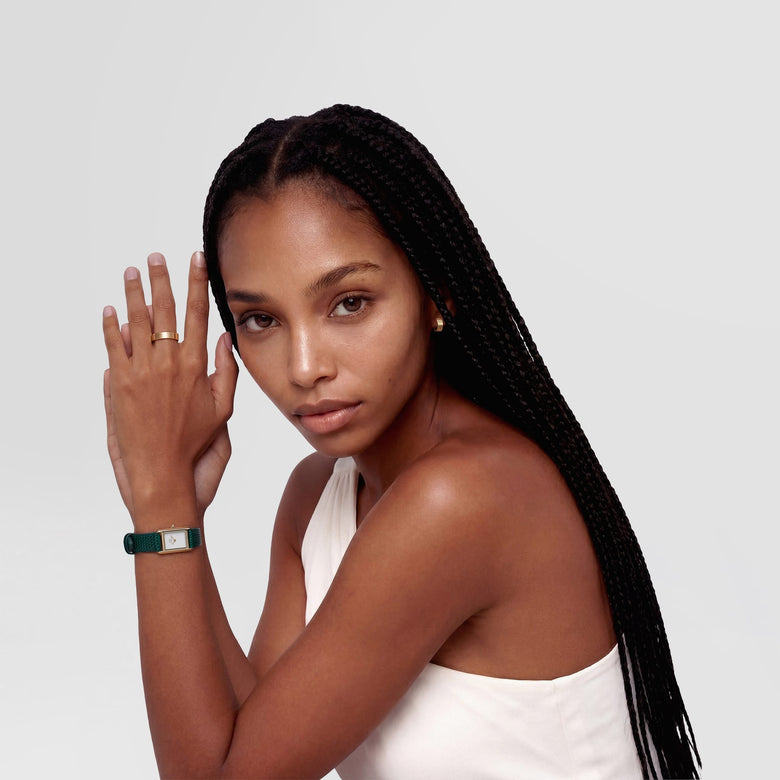 A woman wearing the Line Ring Polished Gold 4.5mm on her finger, styled with a sleeveless white top and a green strap watch, showcasing the ring’s modern gold finish and versatile unisex design for everyday wear.