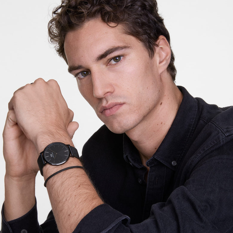 A man wearing the Classic Mesh Onyx Black watch with a black stainless steel mesh strap and minimalist black dial, styled with a black shirt for a modern, versatile look suitable for everyday wear.