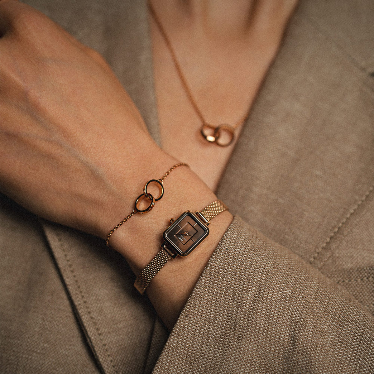 A woman wears the Quadro Mini Melrose Amber with its rose gold mesh strap and amber sunray dial, styled alongside matching rose gold jewellery and a neutral blazer for a sophisticated, everyday look.