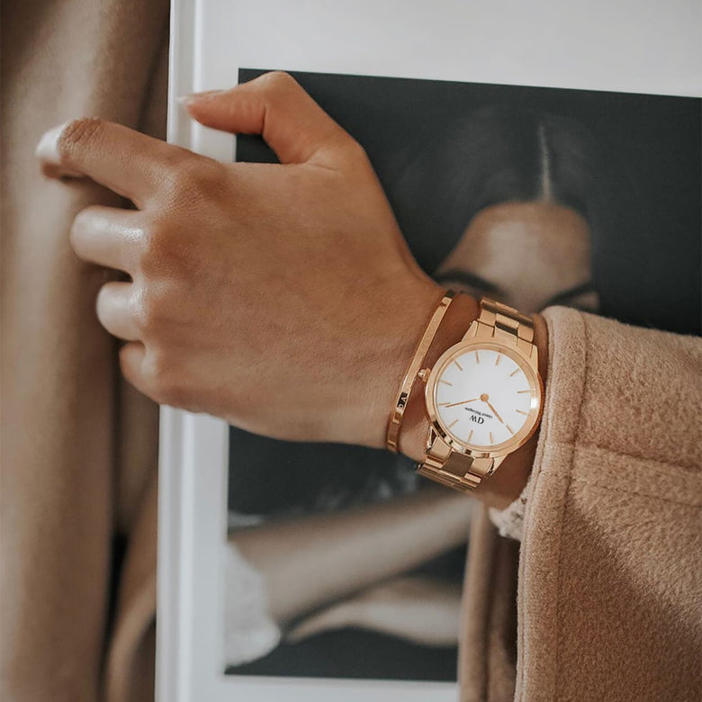 A person wearing the Iconic Link Rose Gold watch with a matching rose gold bracelet, styled with a neutral coat and holding a monochrome art print, highlighting the watch’s minimalist eggshell white dial and polished three-link bracelet.