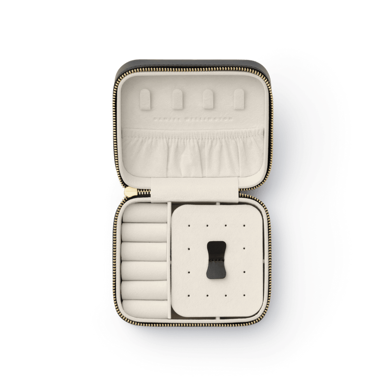 Travel Jewellery Box Black by Daniel Wellington with gold zip, open to display a soft cream interior featuring ring rolls, a pouch pocket, and a removable divider for organised travel accessory storage.