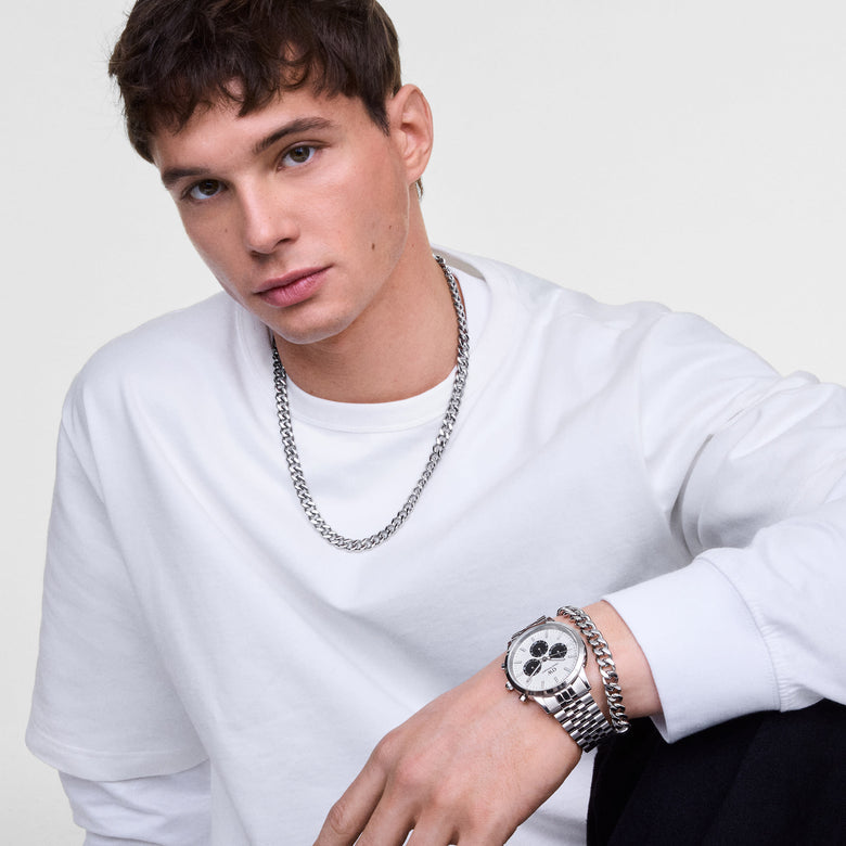 A man wearing the Iconic Chronograph Arch 5-Link Off-White Panda Silver watch, styled with a matching silver chain bracelet and necklace, paired with a white long-sleeve shirt for a modern, casual look.