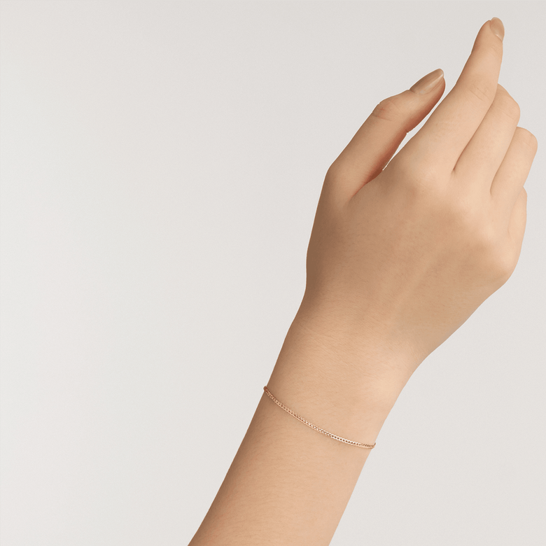 A woman’s wrist wearing the Flat Chain Bracelet G, showcasing its slim, twisted gold chain and minimalist design for an elegant, everyday look.