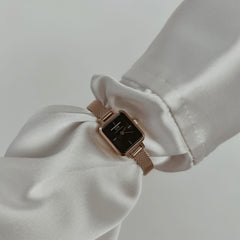 Quadro Mini Melrose Onyx ladies watch with a rectangular black dial and rose gold mesh strap, worn on the wrist with a white long sleeve, showcasing its slim profile and elegant styling for everyday wear.