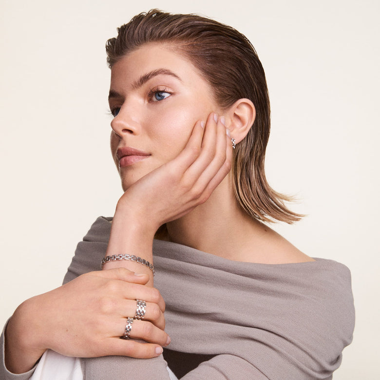 A woman wearing the 3-Link Bracelet Silver on her wrist, styled with matching silver rings and a soft grey top, showcasing the bracelet’s geometric links and polished finish in a modern, elegant look.