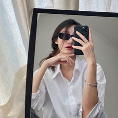 A woman wearing a white shirt takes a mirror selfie, showcasing the Daniel Wellington Emalie Ring Satin White Rose Gold on her finger, styled with a matching rose gold bangle for a modern minimalist look.