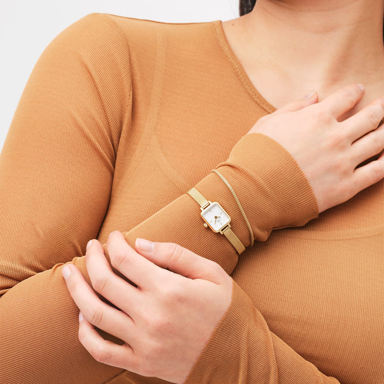 Quadro Mini Evergold gold watch with a petite rectangular case and slim mesh strap, worn on a woman's wrist and styled with a neutral long-sleeve top for a minimalist, everyday look.