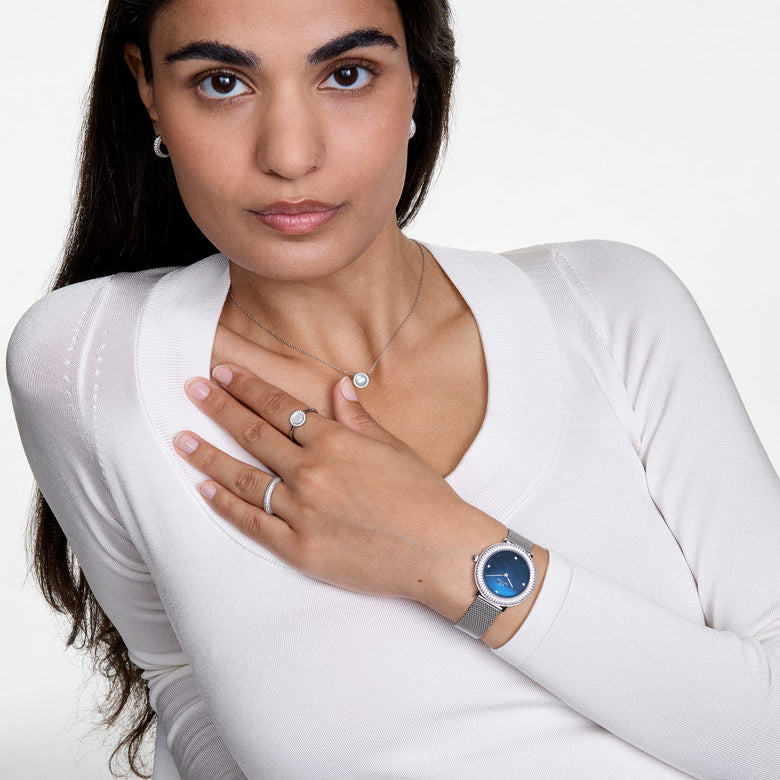 A woman wearing the Audrey Ring Mother of Pearl Silver on her hand, styled with a matching necklace, silver watch, and earrings, showcasing the ring’s luminous mother of pearl centrepiece and halo of cubic zirconia in a coordinated, elegant look.