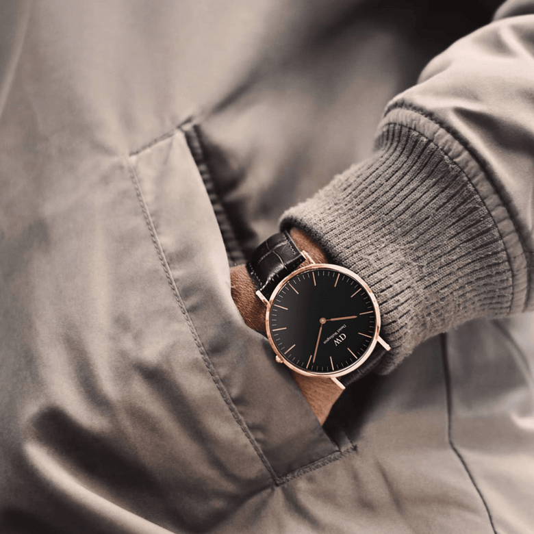A man wearing the Classic York Black Rose Gold watch with a black dial, rose gold case, and dark brown croc-embossed leather strap, styled casually with his hand in a jacket pocket.